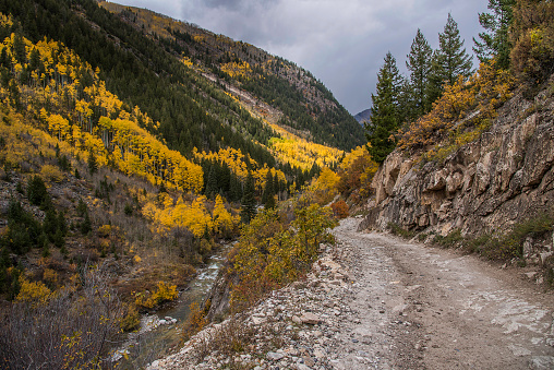 4x4 one lane narrow dirt and rock road in the Rockies in late autumn with snow storm ahead near Aspen, Colorado in western United States of America (USA). A stream flows through the valley to the left over the cliff.