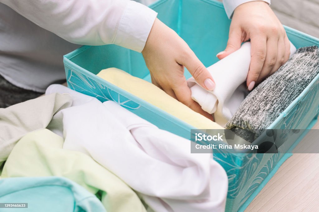 Woman hands folds her clothes and puts them in blue storage box. Vertical storage of clothing, tidying up, room cleaning concept Woman hands folds her clothes and puts them in blue storage box. Vertical storage of clothing, tidying up, room cleaning concept. Adult Stock Photo