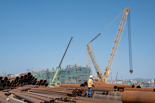 A pile of large steel pipes and working cranes on the chemical construction site