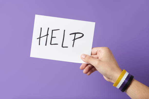 istock Hand with a non binary gender flag bracelet holding a paper with a message: help 1393470395