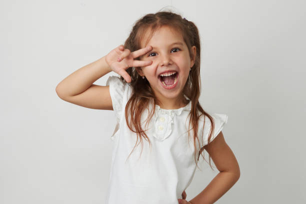 retrato de menina bonita dar v-sign perto do olho - t shirt child white portrait - fotografias e filmes do acervo