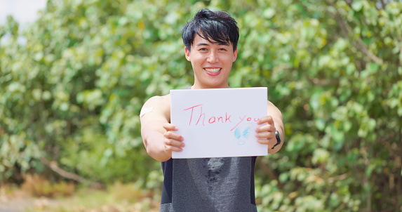 portrait of asian male runner has coronavirus vaccine and he shows his arm with thank you billboard on the road
