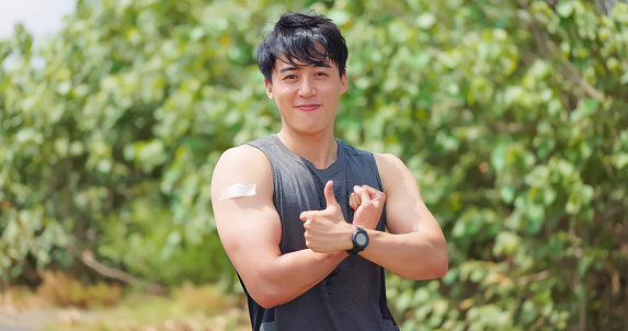 portrait of asian male runner has coronavirus vaccine and he shows his arm with thumb up gesture on the road