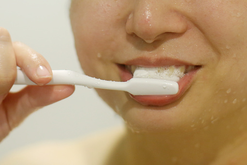An Asian woman is enjoying brushing teeth after shower in bathroom.