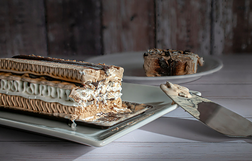A rectangle shape coffee moka ice cream cake on a white plate with a slice served near a wooden rustic wall in the background