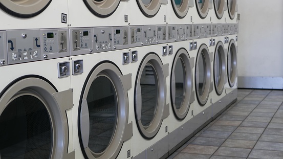 Row of washing and drying machines, public coin laundry in California, USA. Drums of washers and dryers in self-service laundromat or commercial laundrette. Automatic launderette in United States.