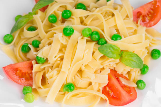 Fettuccine with tomatoes and green peas. Whole background. It occupies the entire surface of the image. Close-up.