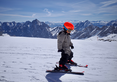 It's Zugspitze, the highest alps in southern Germany. The sky was sunny and blue. The brave little boy was exploring the ski piste.