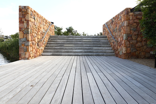 A wooden deck leading up to cement steps with a stone wall on each side.