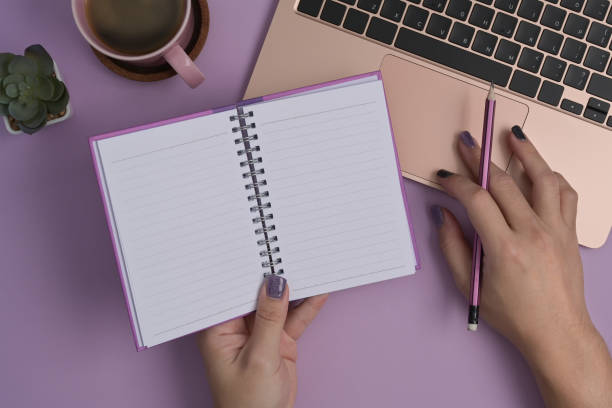 istock Woman holding notepad and using computer laptop on purple background. 1393512670