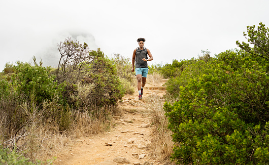 Fit young African man running alone down a scenic trail in some hills in the early morning