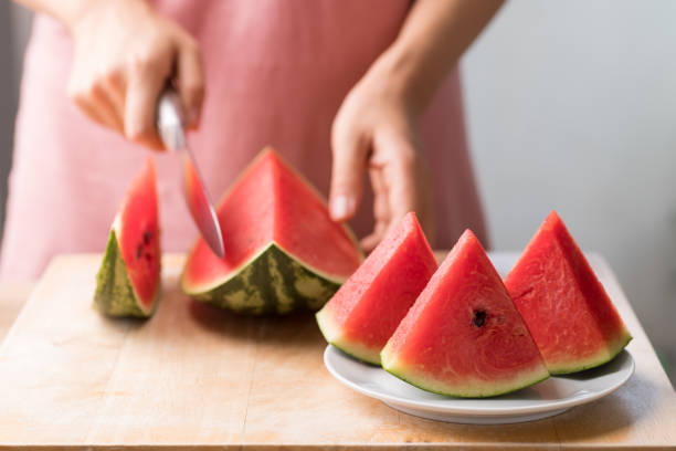 istock Hand holding knife and cutting watermelon on wooden board 1393514751