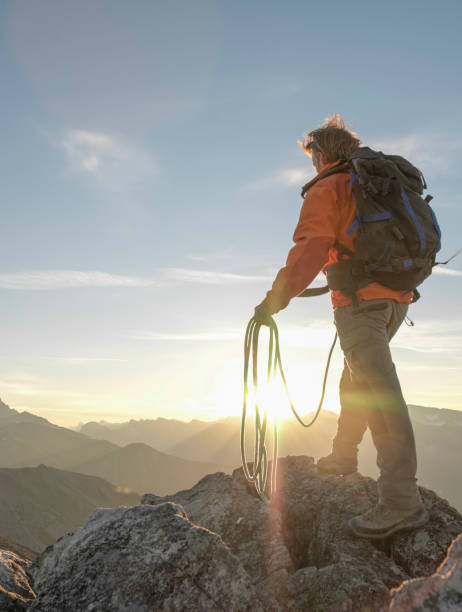 Mountaineer prepares to throw rope from summit, sunset