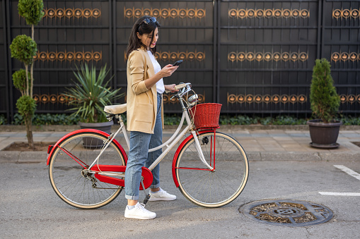Side view of young female tourist using phone while exploring city on vintage bicycle