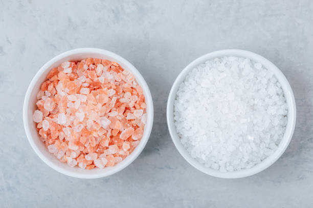 himalayan crystal salt in white bowls on gray stone background. - salt crystal spoon food imagens e fotografias de stock