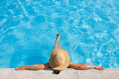 top view of woman in straw hat relaxing in swimming pool on resort. Summer vacation idyllic background