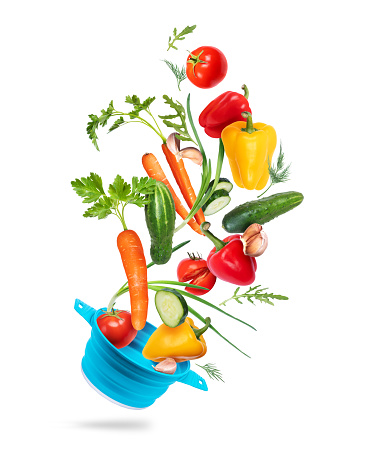 Different vegetables fly out from plastic bowl on a white background