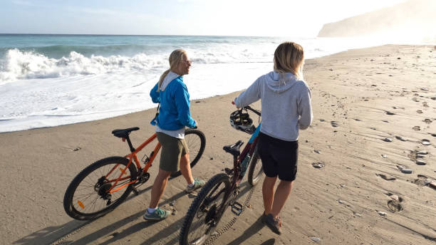 istock Women push mountain bikes down beach 1393520859