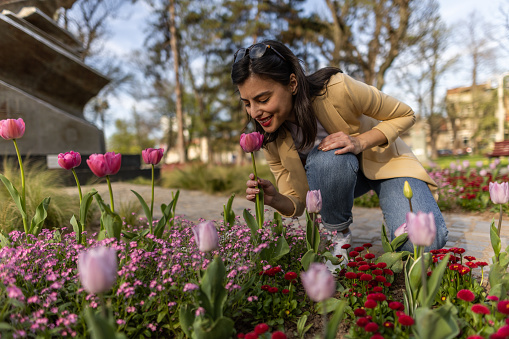 Beautiful young woman smelling tulips in city garden on sunny spring day