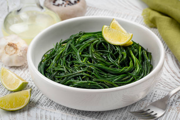 Close up of Sauteed Agretti with lemon, italian food. Saltwort or salsola soda on a white table. stock photo