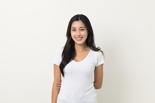 Beautiful young asian woman age around 25 smiling wearing white shirt. Charming female standing on isolated white background. Asian people pose looking camera with white backdrop.