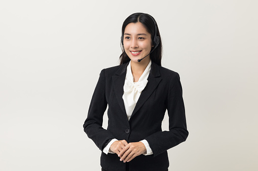 Happy young asian business woman call centre. Welcome female operator put on smalltalk headphone standing on isolated white background.