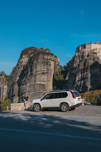 Greece car travel concept. Man standing near suv looking at meteora monastery thessaly mountains