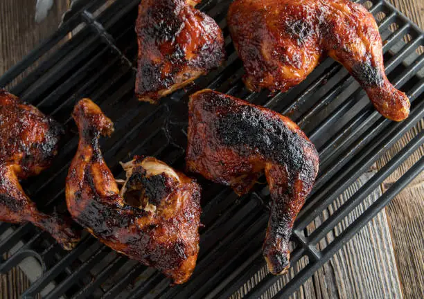 Fresh grilled marinated and honey glazed chicken legs. Served on a grill grate on wooden table background. Closeup and overhead view