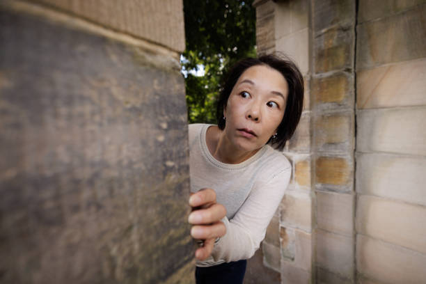 Scared woman looking around a corner Woman with a scared expression looking around the corner of a stone wall. looking around stock pictures, royalty-free photos & images