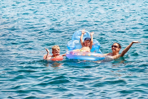 Mother and kids have fun swimming in blue water of sea in Marmaris. Woman with preschooler and toddler in rubber rings enjoys summer vacation in Turkey