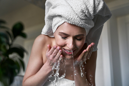 Front view of woman washing face with water in the bathroom