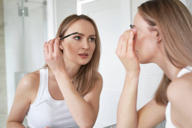Young caucasian woman brushing eyebrows in the mirror reflection stock photo