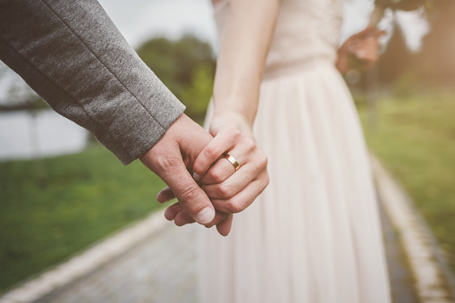 Bride and groom holding hands with golden rings outdoors