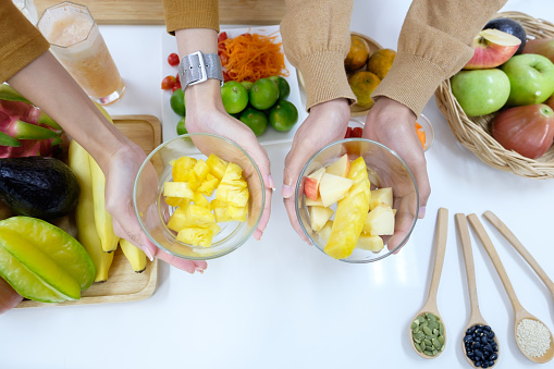 Top view of the couple's hand holding the fruit bowl and there are many fruits on the table. Food for health lovers concept.