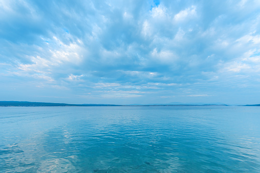 Tranquil sea water surface with rippled reflection of the clouds and sky as natural background