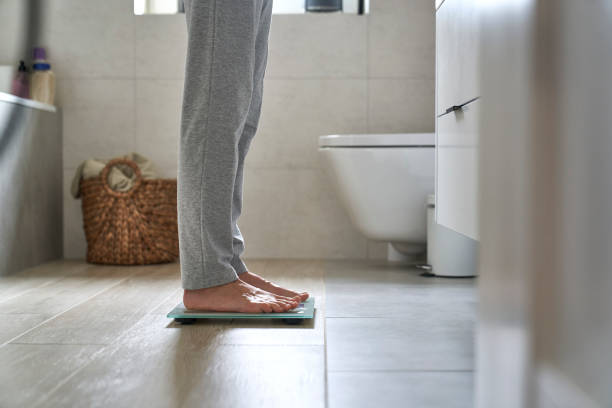 Legs of unrecognizable woman standing on the bathroom scale stock photo