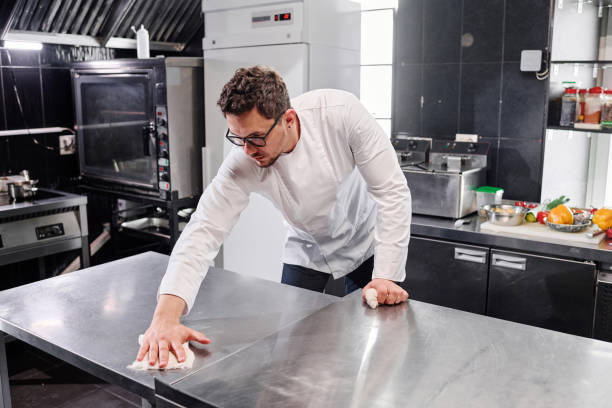 The cook cleaning kitchen after cooking Young professional cook in uniform wiping kitchen counter in kitchen after cooking commercial kitchen photos stock pictures, royalty-free photos & images