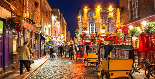 Panorama of Dublin night street in Temple Bar area, nightlife in Ireland Dublin, Ireland - 15 June, 2021: Panoramic view of night old town in Temple Bar area, young people walking on busy night street with pubs and bars friday stock pictures, royalty-free photos & images
