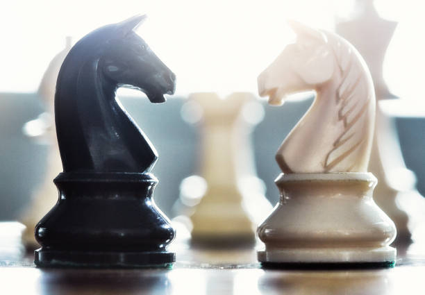 Ethereal close-up of black and white knights facing each other on a chessboard.