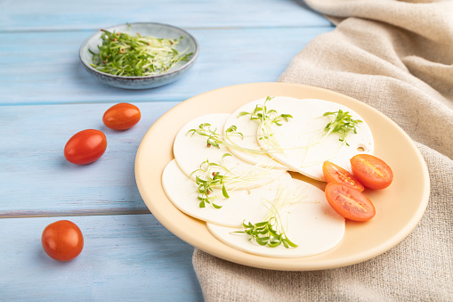 White cheese with tomatoes and cilantro microgreen on blue wooden background and linen textile. side view, close up.