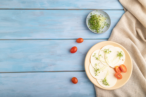 White cheese with tomatoes and cilantro microgreen on blue wooden background and linen textile. top view, flat lay, copy space.