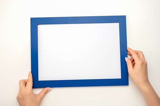 Holding frame mockup. incline Photo Mockup. Woman hands hold blue frame. Frame size A4. isolated on white background. blank photo frame border with copy space in hands close up