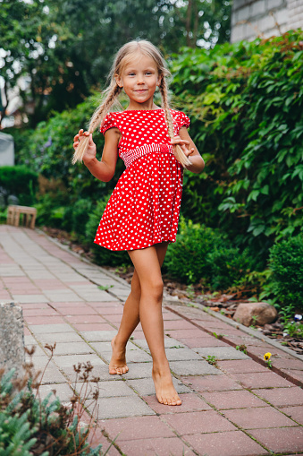 happy little girl in red dress with pigtails walking in the garden. Summer holidays.