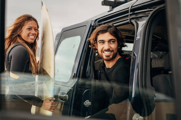 pareja con tabla de surf en traje de neopreno, preparándose en el coche para ir a la playa - women sea cheerful surfing fotografías e imágenes de stock