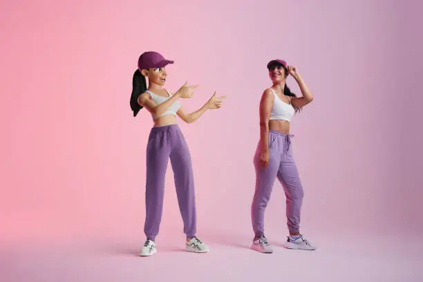 Cheerful young woman smiling at her metaverse avatar in a studio. Happy young woman standing next to the 3D simulation of herself. Sporty young woman exploring virtual reality.