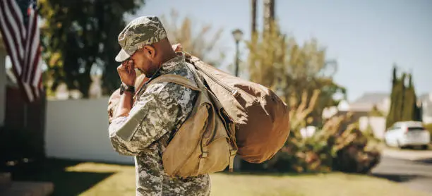 American soldier walking towards his house with his luggage. Emotional serviceman coming back home after serving in the military.