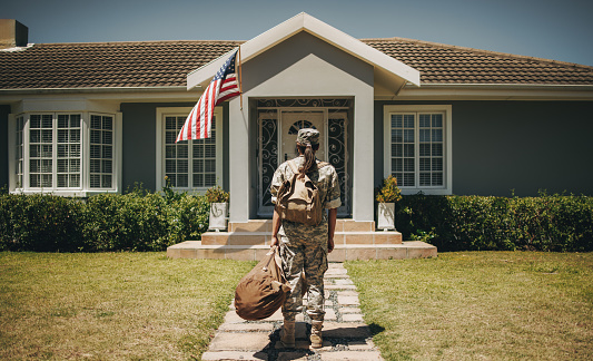 Rearview of a patriotic female soldier standing in front of her home with her luggage. Courageous servicewoman coming back home after serving her country in the military.