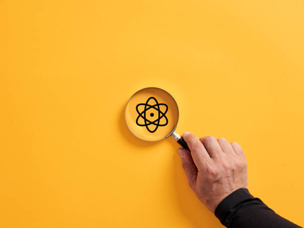 Hand holding a magnifier over the atom symbol. Science and scientific research concept.