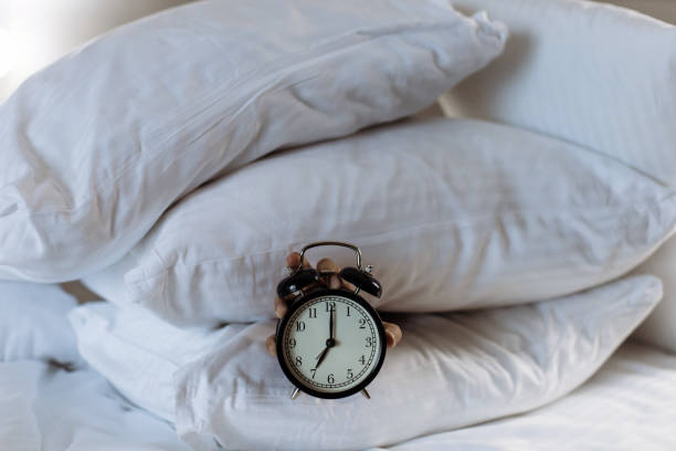 istock Hand keeps alarm clock with seven o clock on it. Hand surround with pillows on the bed 1393558155