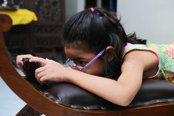 Asian kid girl using mobile phone gadget when lying in the couch Asian kid girl using mobile phone gadget when lying in the couch keluarga stock pictures, royalty-free photos & images